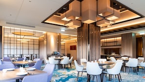 A modern hotel dining area with round tables, white chairs, and a blue patterned carpet. - Howard Prince Hotel Taichung (Taichung)