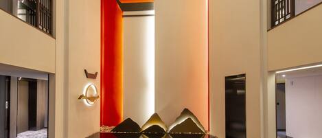 A modern hallway with a reflective floor, a red accent wall, and a decorative wall piece.