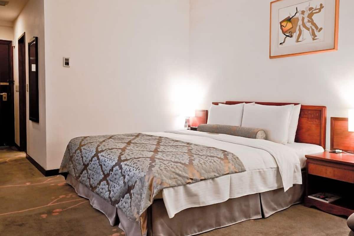 Habitación de hotel con una cama grande, una mesita de noche, un cuadro enmarcado en la pared y piso alfombrado.