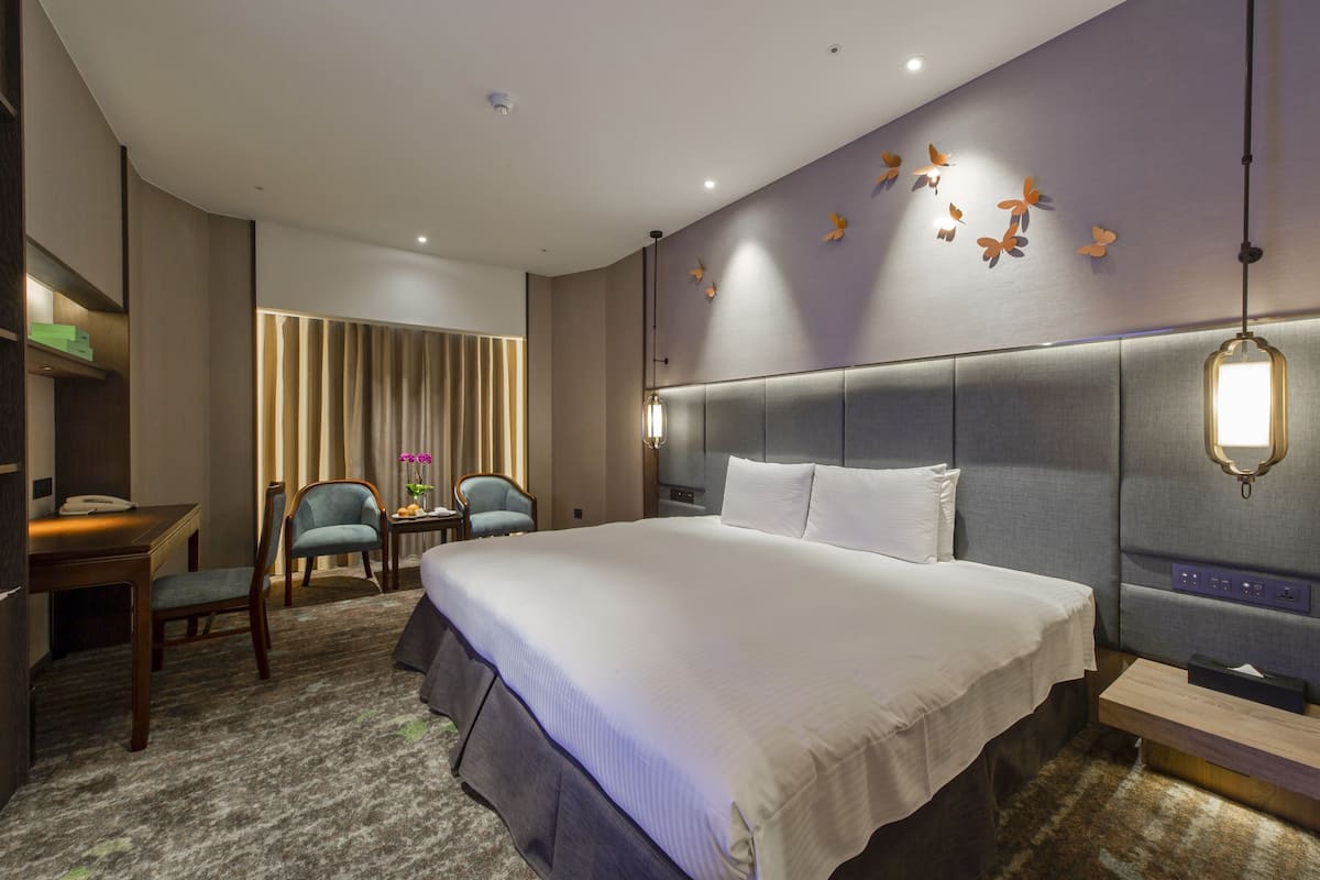 Una habitación de hotel moderna con una cama grande, un escritorio, dos sillas y un muro decorativo con motivos de mariposas.