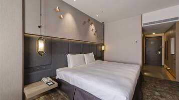 A hotel room with a large bed, bedside lamps, a phone on a nightstand, and a wall-mounted light fixture.