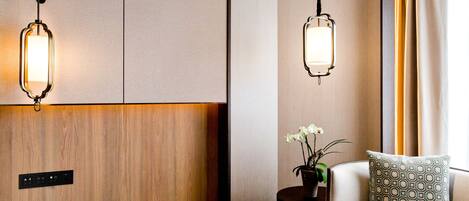 Una habitación de hotel moderna con un mostrador de recepción de madera, un sofá con cojines estampados y dos lámparas colgantes.