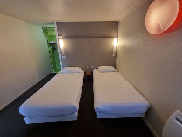 Quarto de hotel com duas camas de solteiro, parede verde e luminária vermelha.
