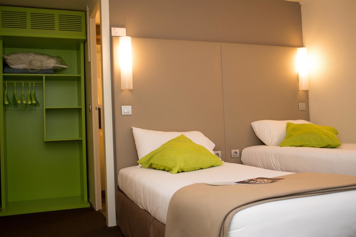A hotel room with two beds, a green wardrobe, and wall-mounted lights.