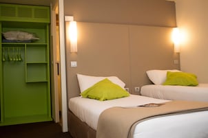 Quarto de hotel com duas camas, um guarda-roupa verde e luminárias fixadas na parede.