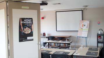 Een vergaderzaal met tafels, stoelen, een projectiescherm en een poster aan de muur.