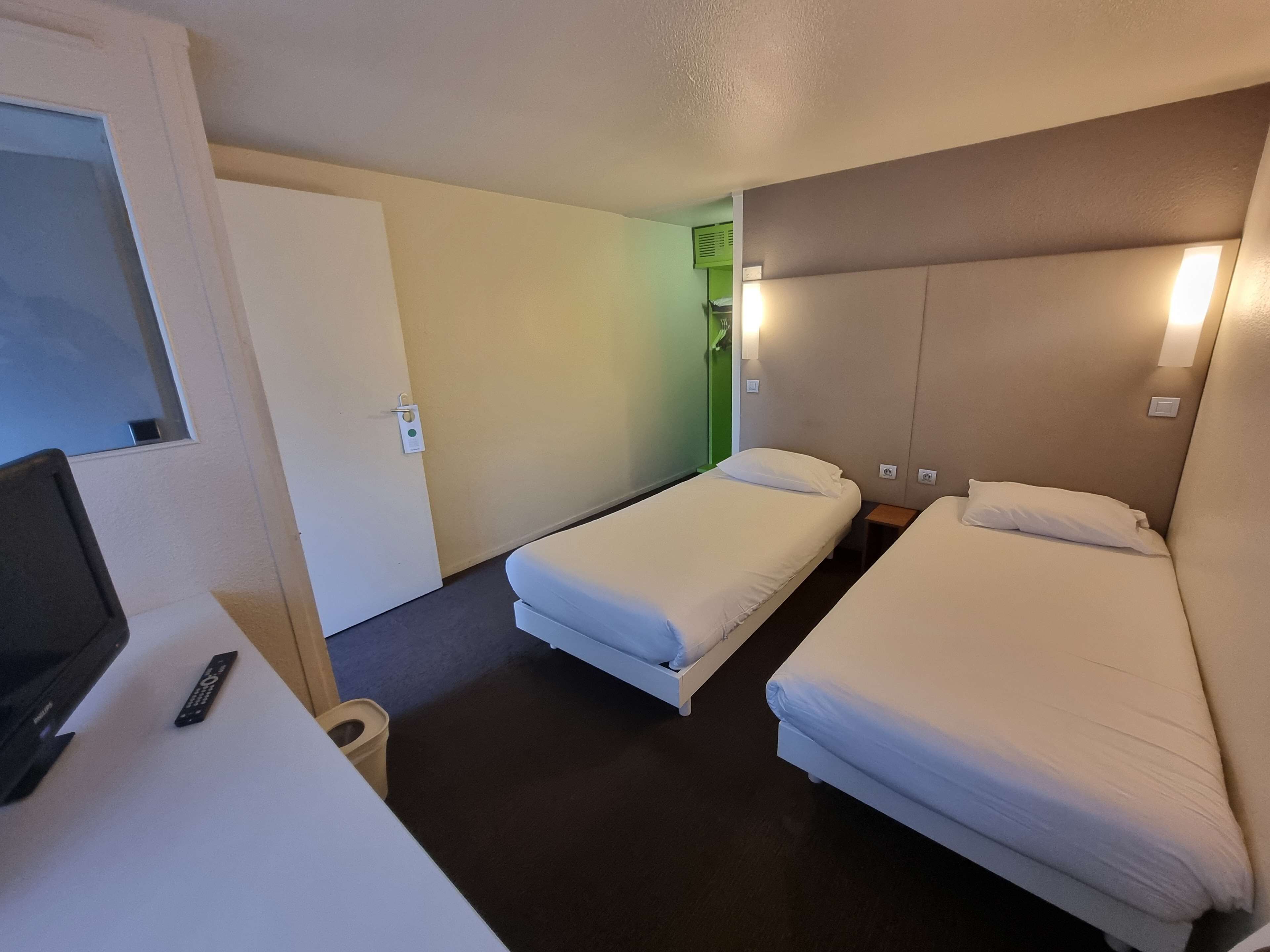 Une chambre d’hôtel avec deux lits simples, un bureau avec une télévision et une porte dotée d’un voyant lumineux vert.