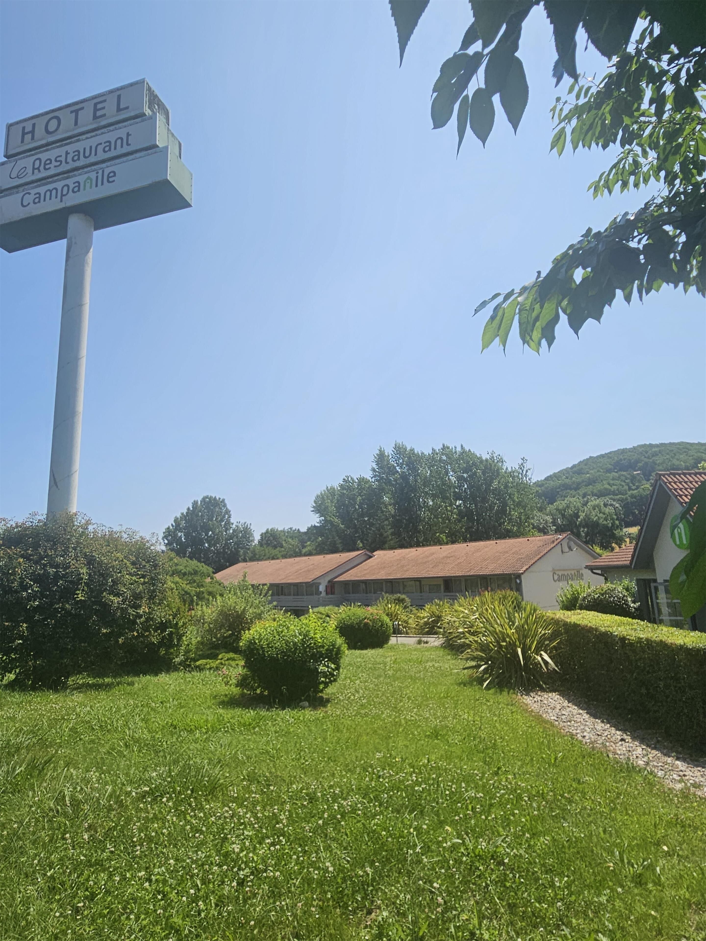 A signpost with "HOTEL," "Restaurant," and "Campanile" written on it, with a building in the background.