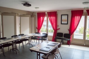 Uma sala de conferências com uma mesa comprida, cadeiras, um projetor e cortinas vermelhas.