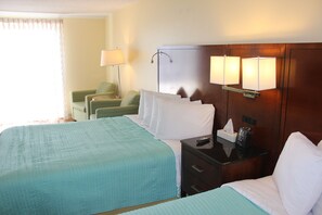 A hotel room with a bed, a nightstand, a lamp, a chair, and a window with curtains.