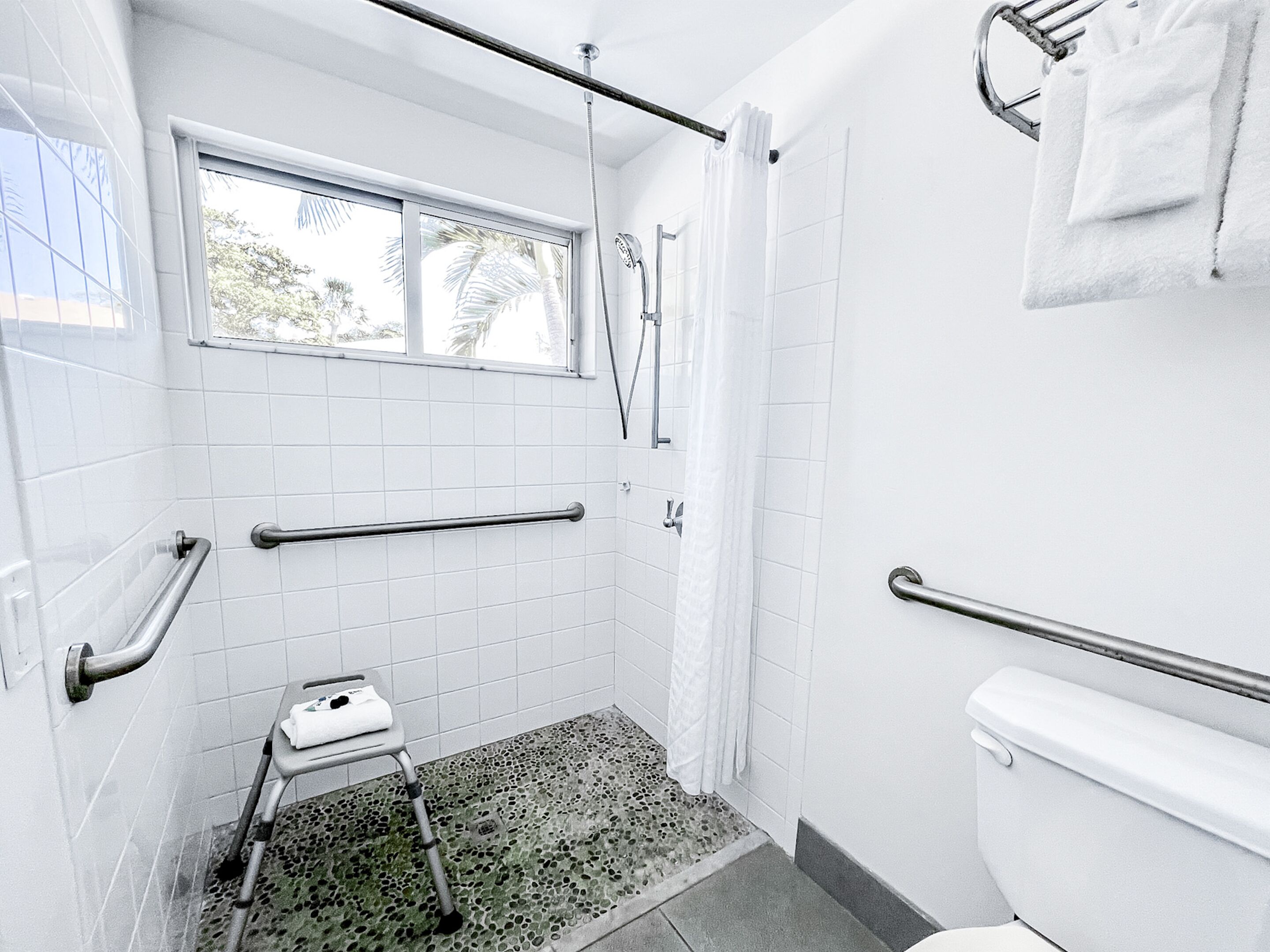 A bathroom with white tiles, a shower, a toilet, and a window.