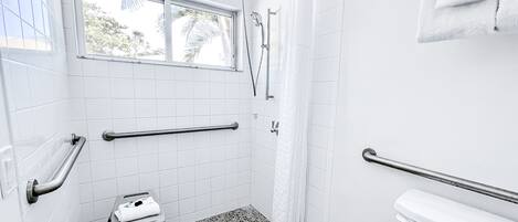 A bathroom with white tiles, a shower, a toilet, and a window.