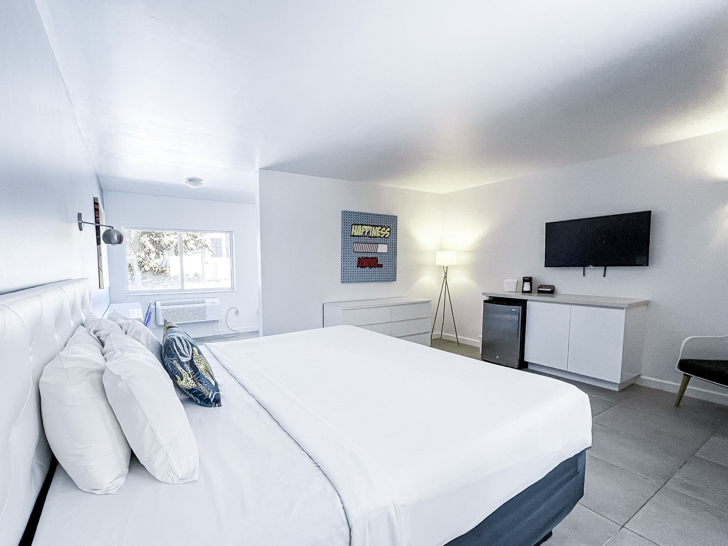 A modern hotel room with a large bed, a desk, a flat-screen TV, and a window with a view of trees.