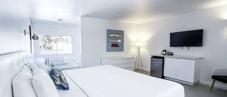 A modern hotel room with a large bed, a desk, a flat-screen TV, and a window with a view of trees.