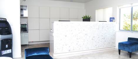 A modern reception area with a marble counter, blue upholstered chairs, and a view of the outdoors through large windows.