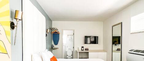 Una habitación de hotel moderna con cama, escritorio, televisión y espejo.