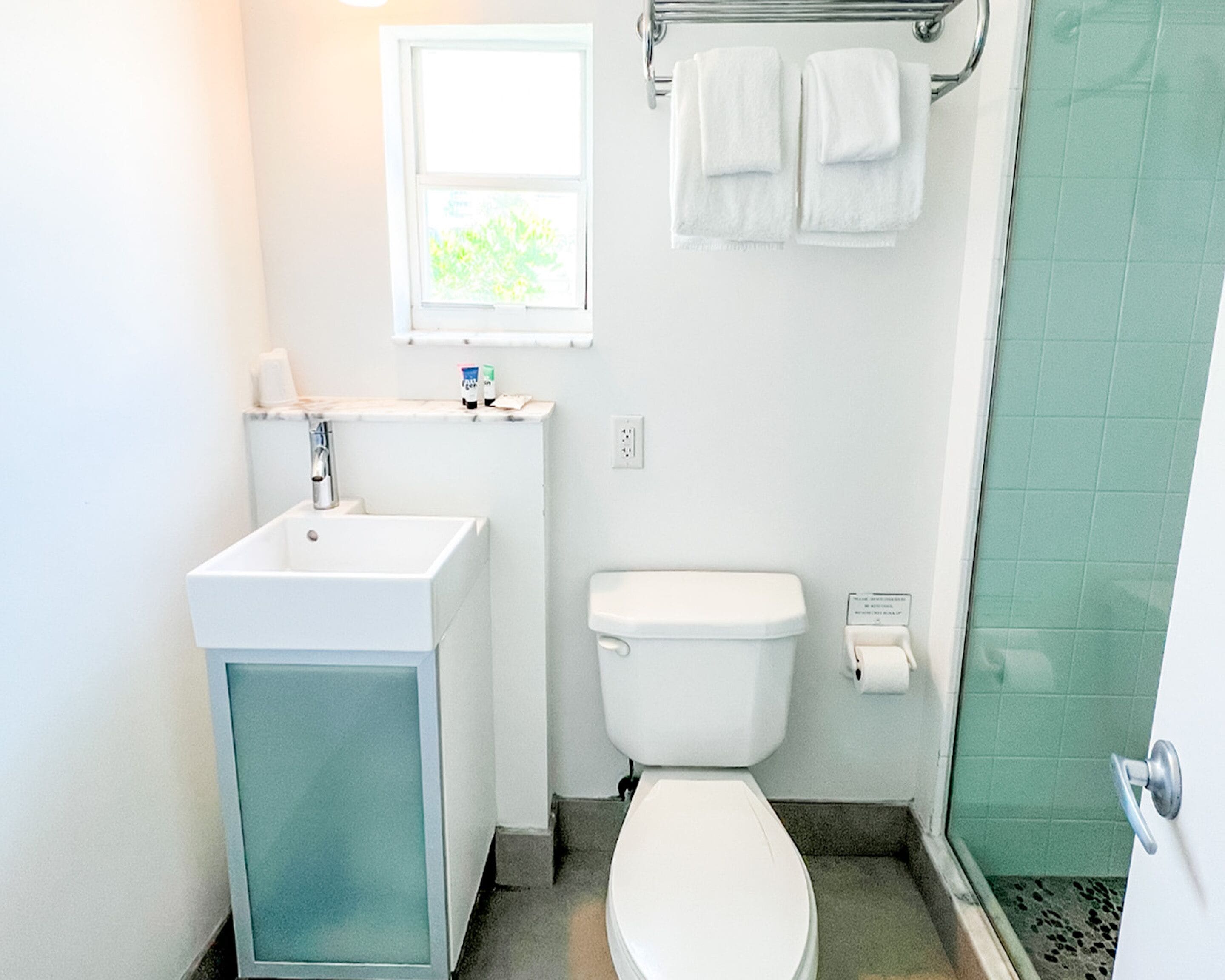 A small bathroom with a white sink, toilet, and a window above the sink.
