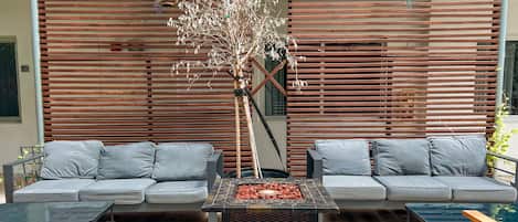 An outdoor seating area with two grey sofas, a glass-top table, and a decorative tree.