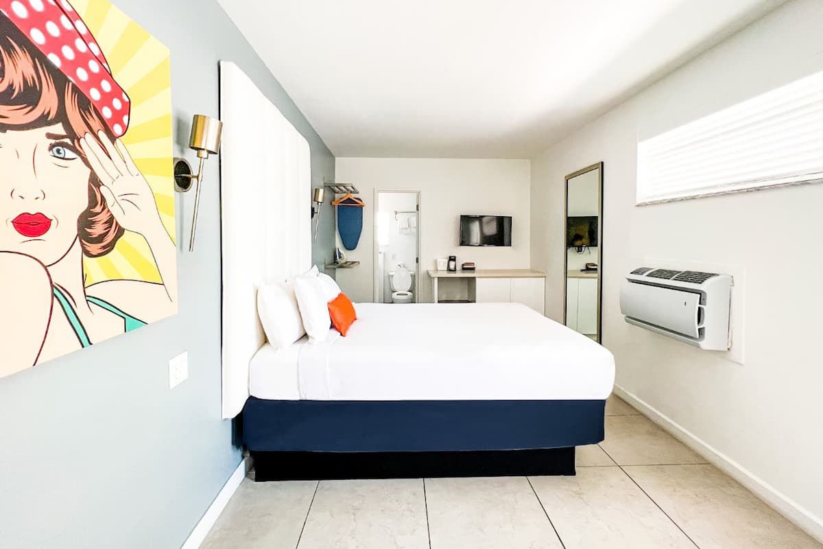A hotel room with a bed, a TV, a mirror, and a window.
