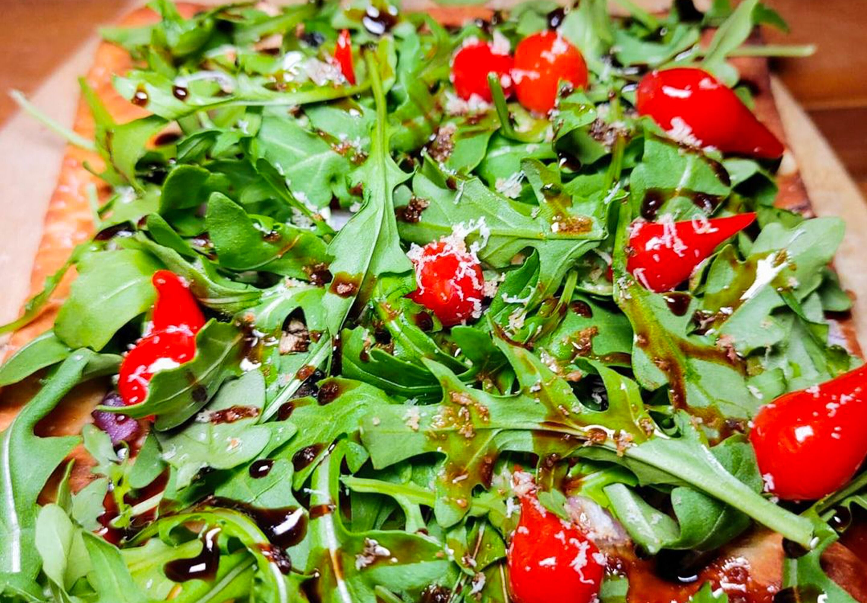 Ein Nahaufnahme eines Salats mit Rucola, Cocktailtomaten und Balsamico-Glasur.