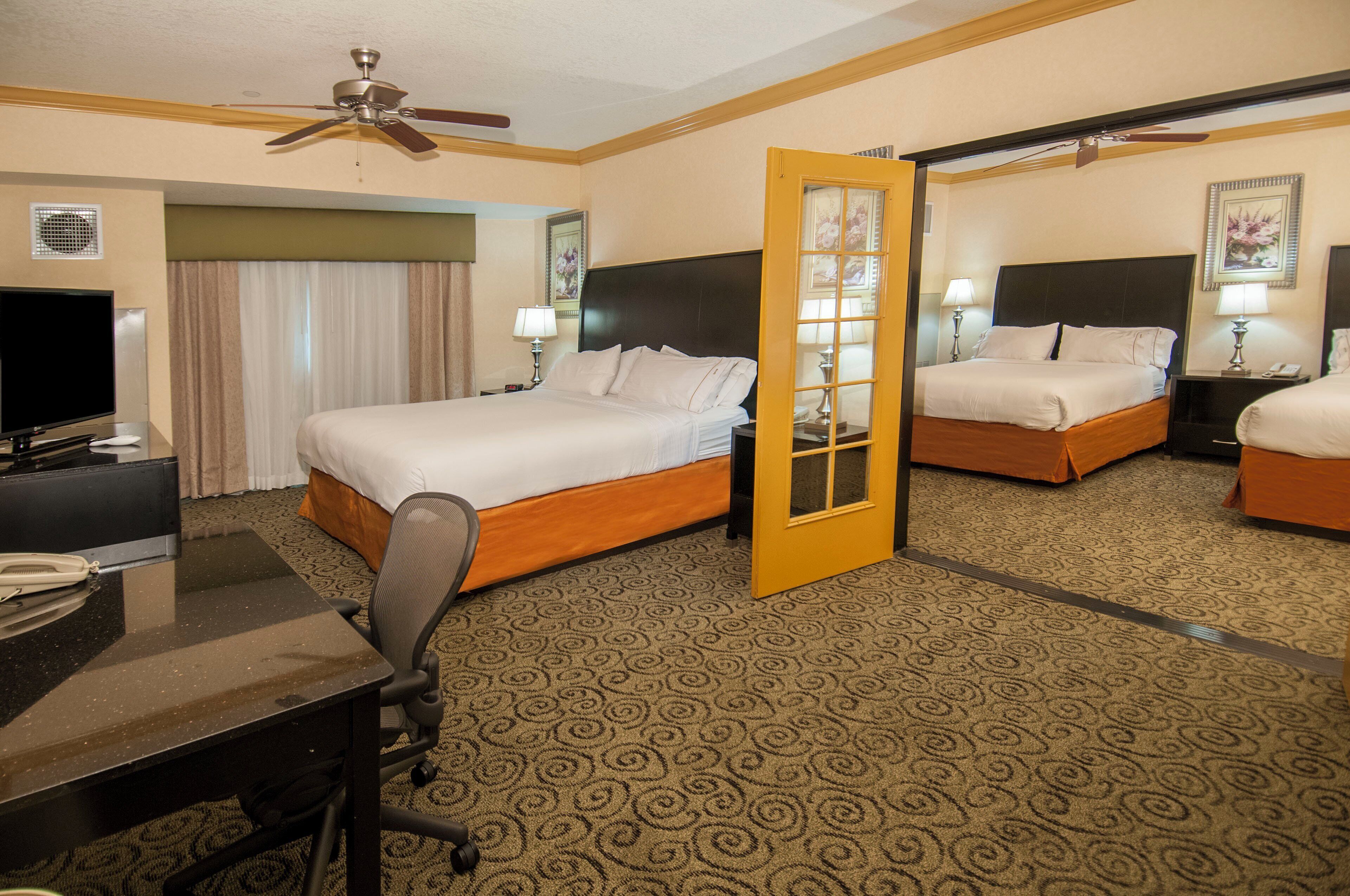 A hotel room with a bed, desk, chair, television, and a door leading to another room.
