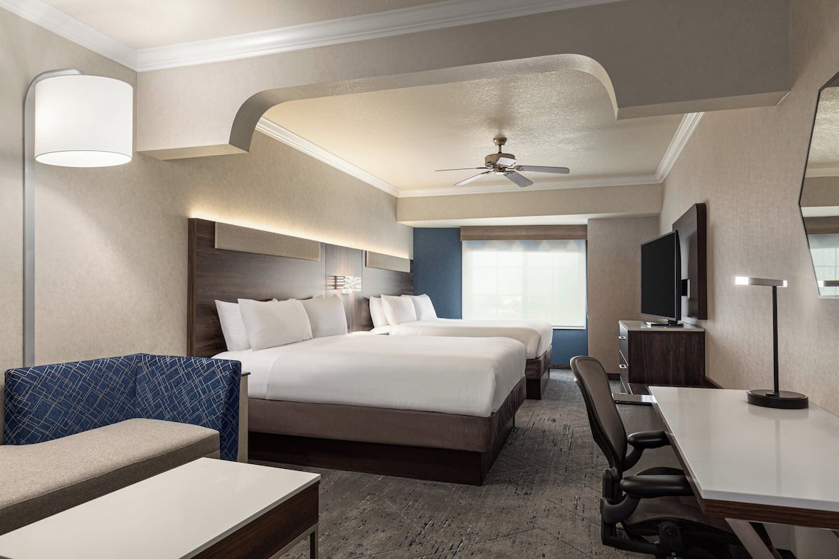 A hotel room with a large bed, a desk, a chair, a TV, and a ceiling fan.