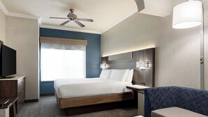 A hotel room with a bed, a desk, a television, a ceiling fan, a window, and a wall-mounted lamp. - Holiday Inn Express and Suites Bakersfield Central by IHG (Bakersfield)