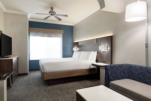 A hotel room with a bed, a desk, a television, a ceiling fan, a window, and a wall-mounted lamp. - Holiday Inn Express and Suites Bakersfield Central by IHG (Bakersfield)