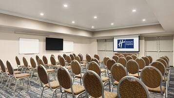 A conference room with rows of chairs, a projection screen, and a Holiday Inn Express sign.
