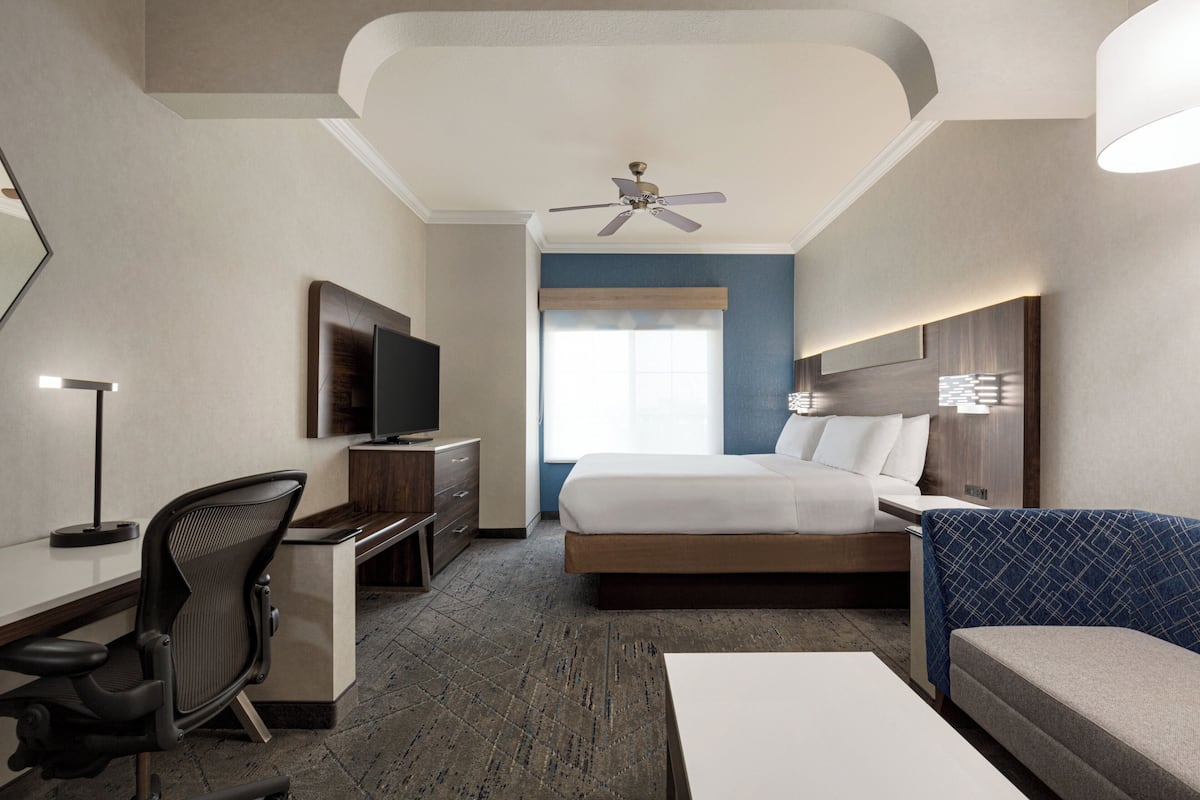 A hotel room with a bed, desk, chair, television, and a ceiling fan.