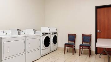 A laundry room with a washing machine and dryer, two chairs, and a table.