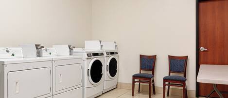A laundry room with a washing machine and dryer, two chairs, and a table.