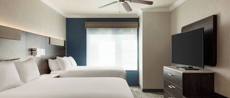 A hotel room with two beds, a ceiling fan, a flat-screen TV, and a large window with blinds.