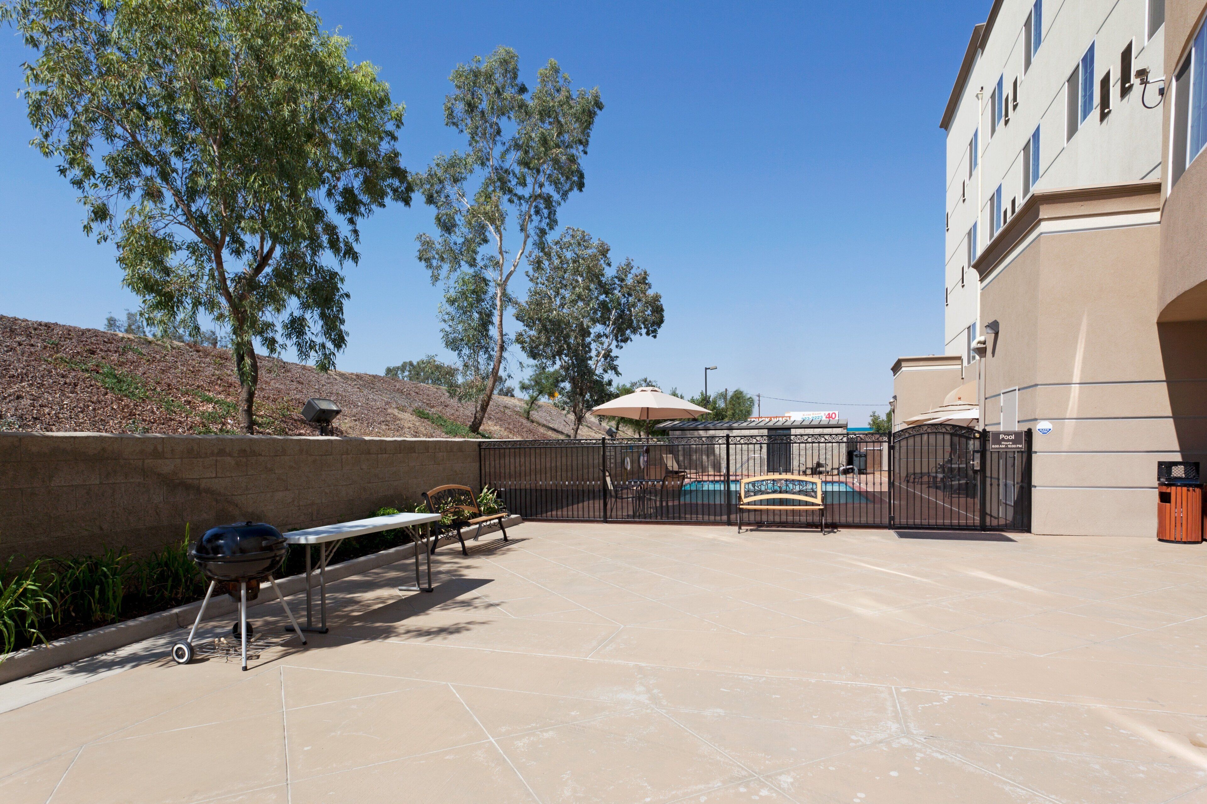 An outdoor patio with a barbecue grill, a pool, and a fence.