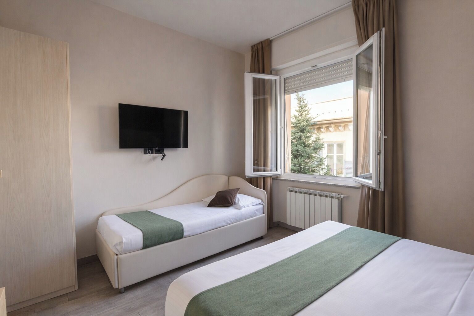 Una habitación de hotel con cama, sofá cama, televisor y ventana con cortinas.