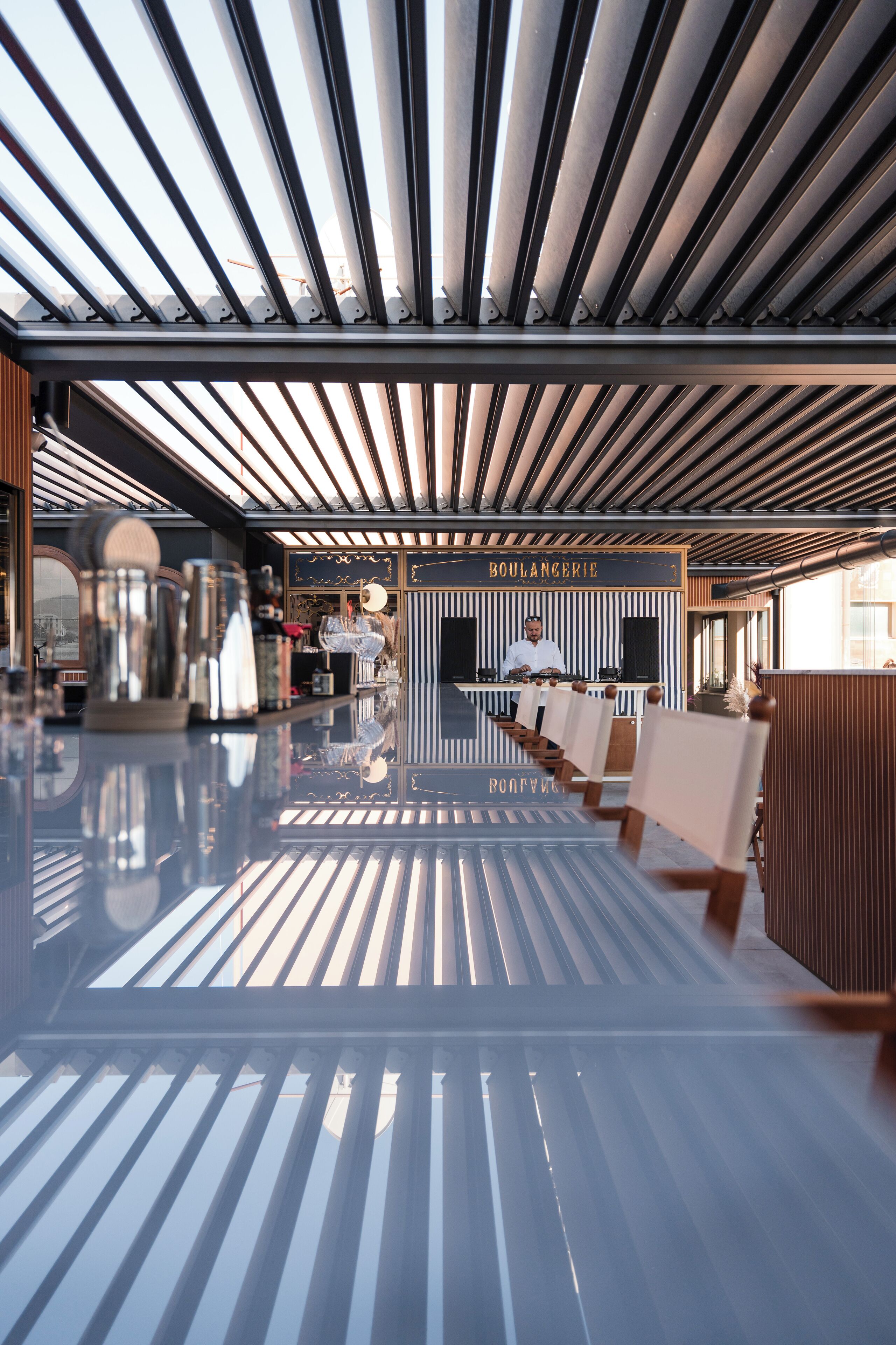 A modern interior with a reflective floor, a bar area with a chef, and a sign reading "BOULANGERIE".