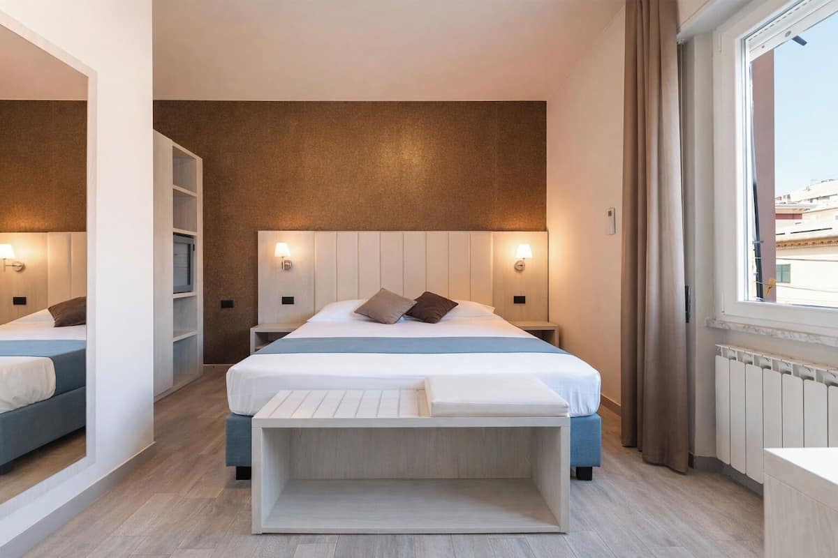 Una habitación de hotel moderna con una cama grande, mesitas de noche con lámparas, un banco integrado y vistas por la ventana.
