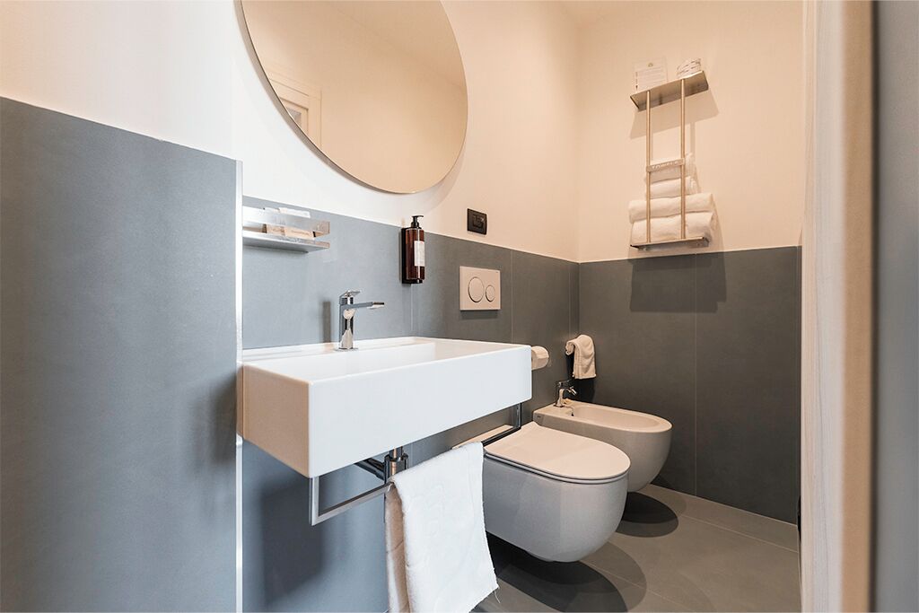 Een moderne badkamer met een wit wastafel, een ronde spiegel, een toilet en een handdoekhouder.