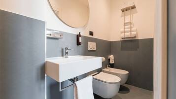 Een moderne badkamer met een wit wastafel, een ronde spiegel, een toilet en een handdoekhouder.