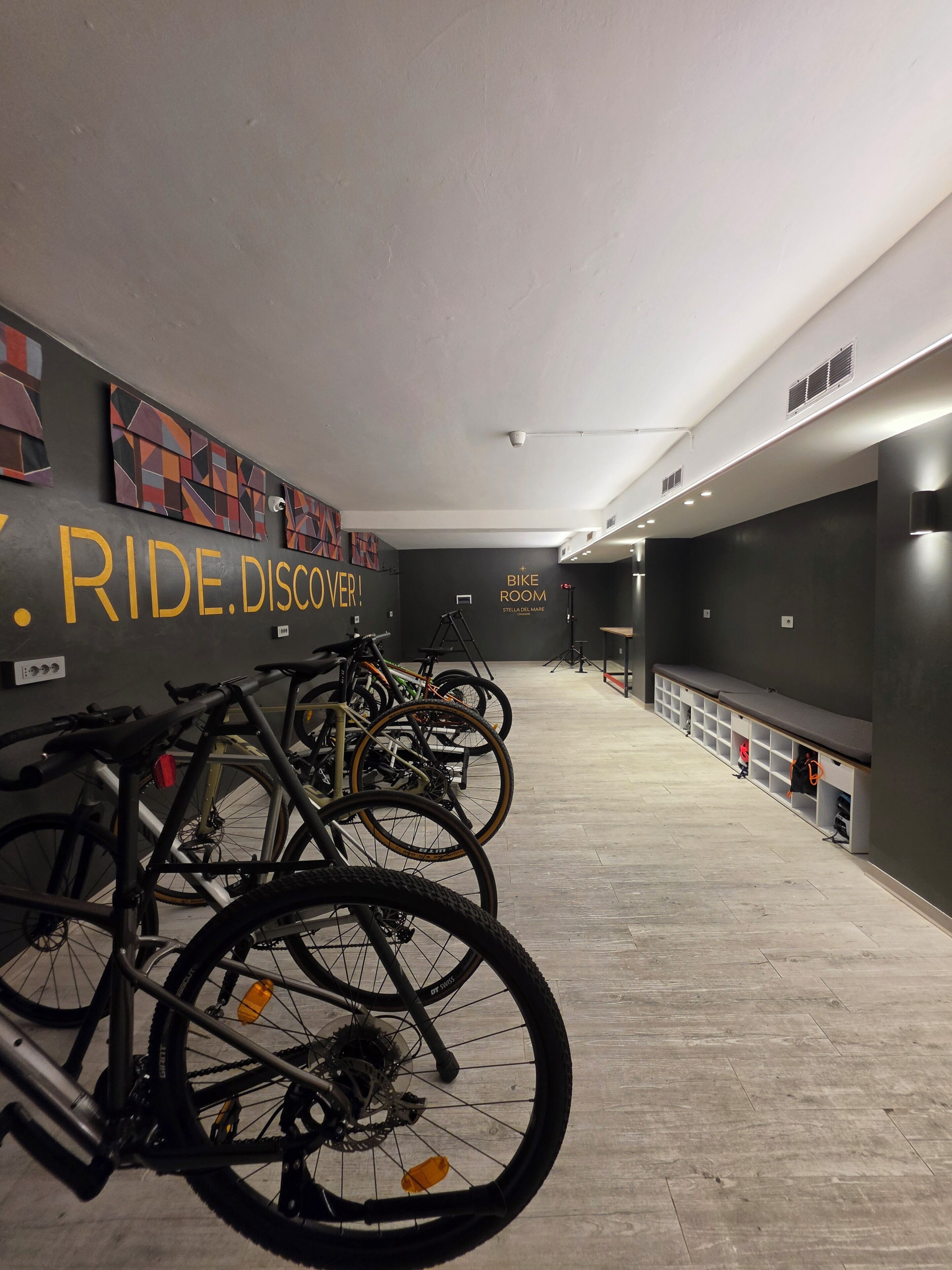 A bike room with bicycles parked against the wall, a sign reading 'BIKE ROOM,' and a wall with abstract art.