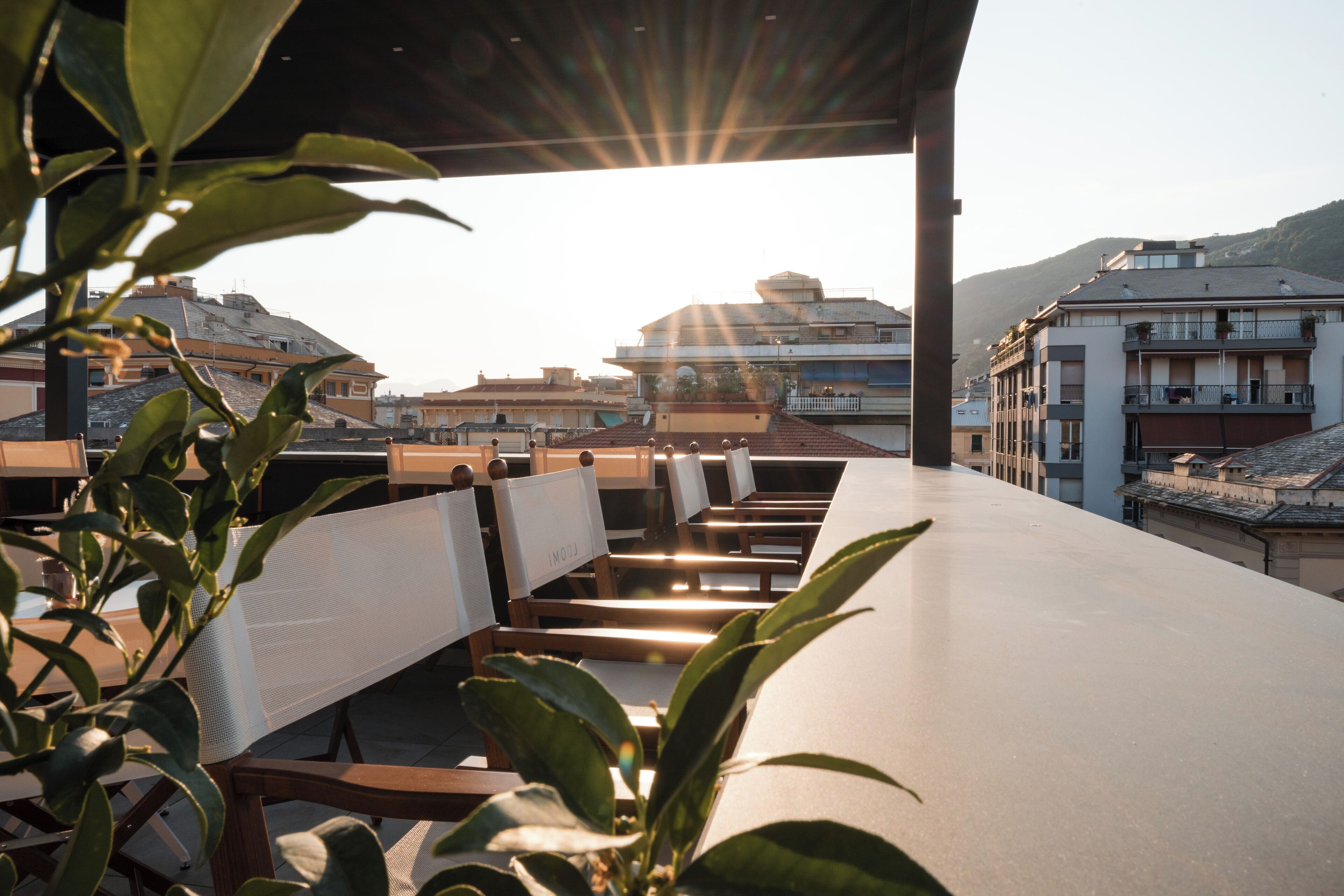An outdoor seating area with tables and chairs, overlooking a cityscape with buildings and hills.