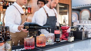 A bar setting with a bartender pouring a drink, glasses of beverages, and bottles of Coca-Cola and other drinks on the counter. - Albergo Stella Del Mare (Chiavari)