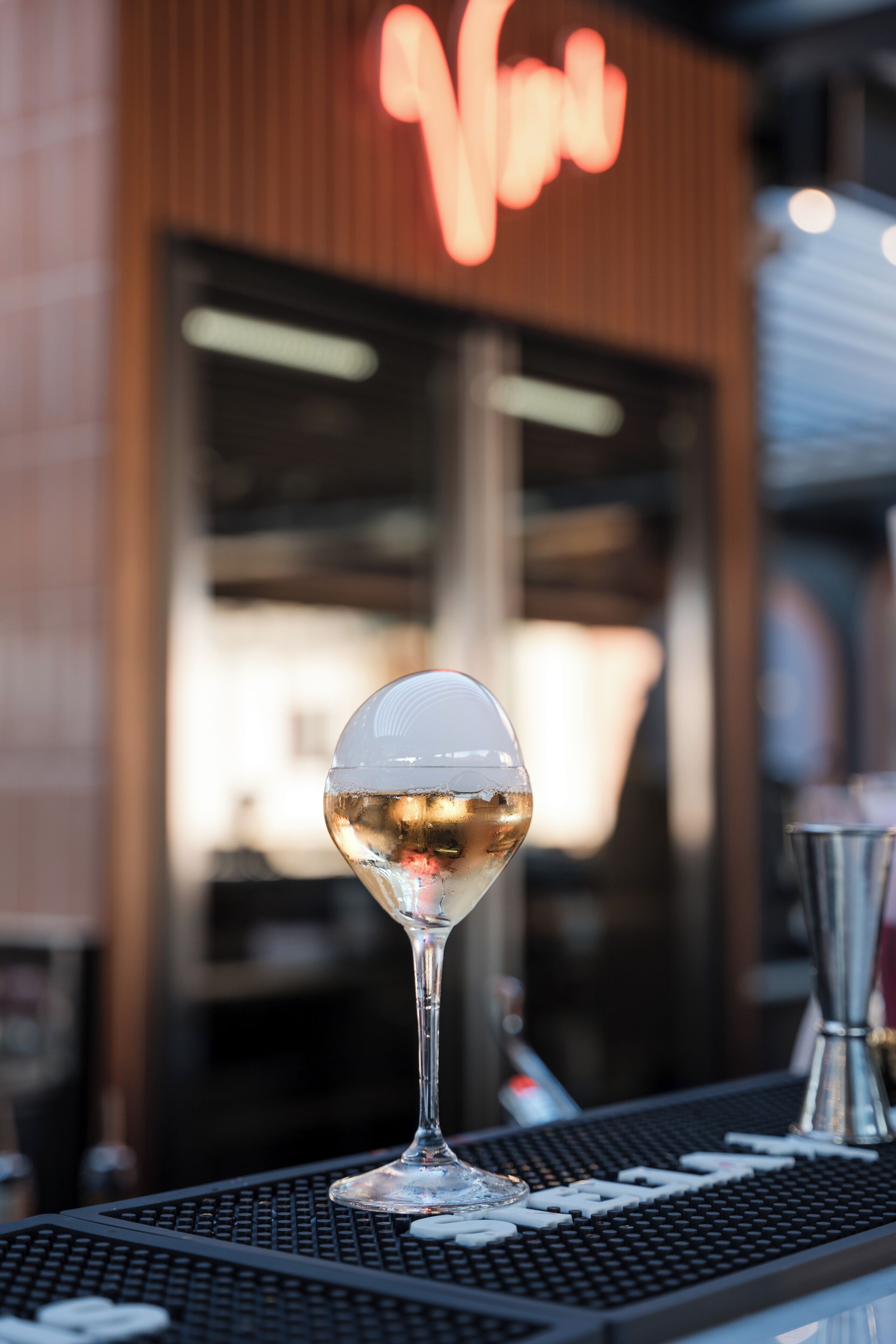 A bar setting with a clear glass of a white beverage, a barista machine, and a neon sign in the background.