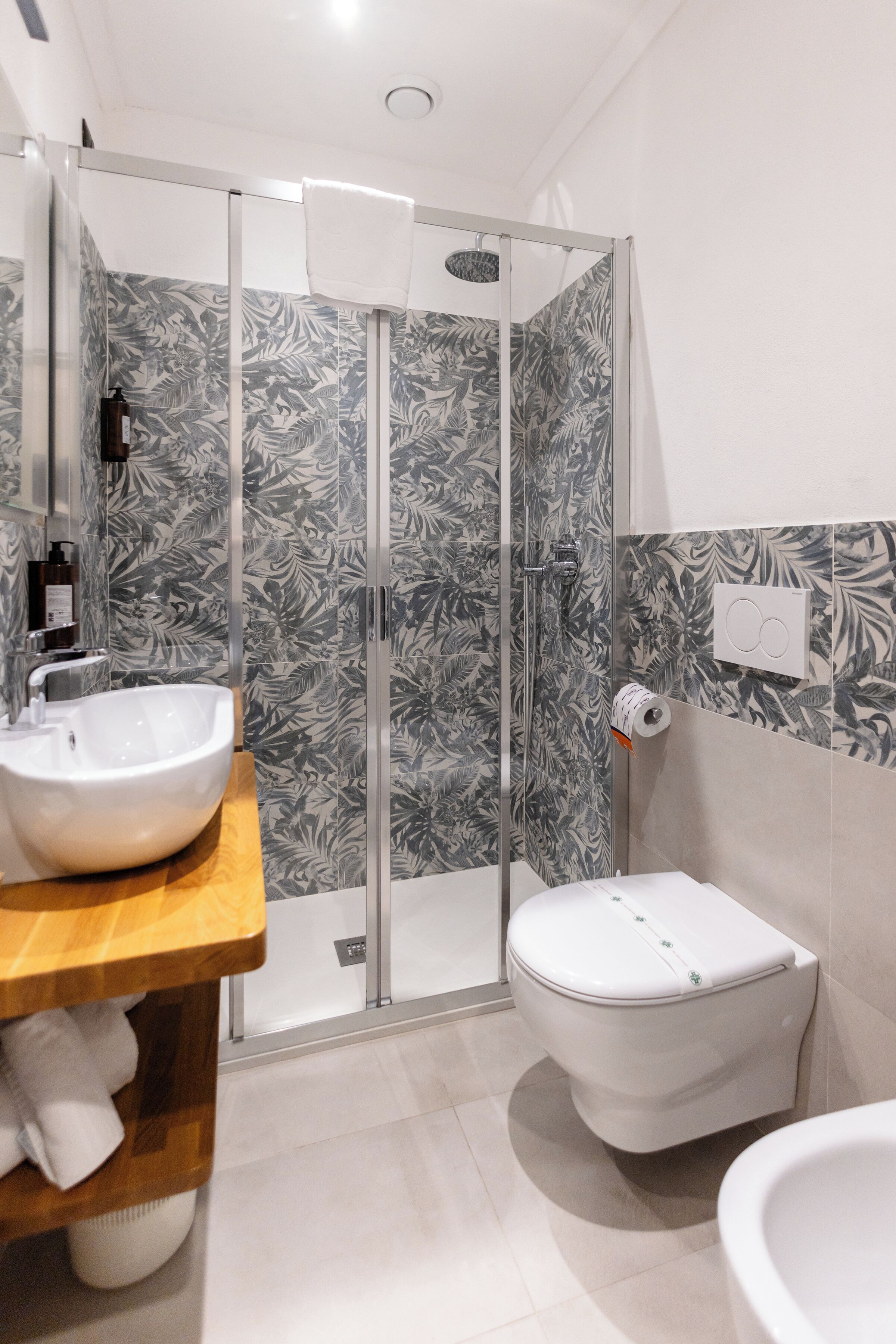 A modern bathroom with a glass shower enclosure, a wooden vanity with a white sink, and a white toilet.