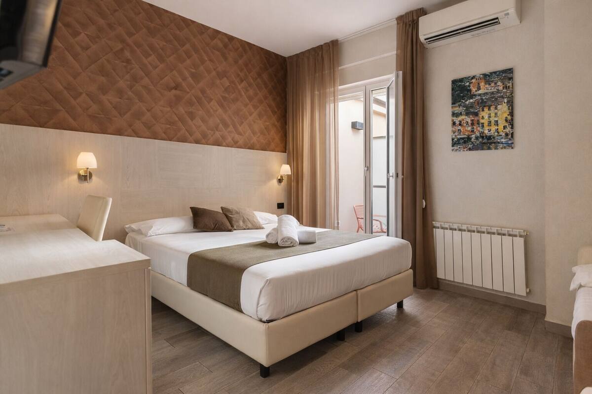 Una habitación de hotel con una cama, mesitas de noche, un radiador y un cuadro en la pared.