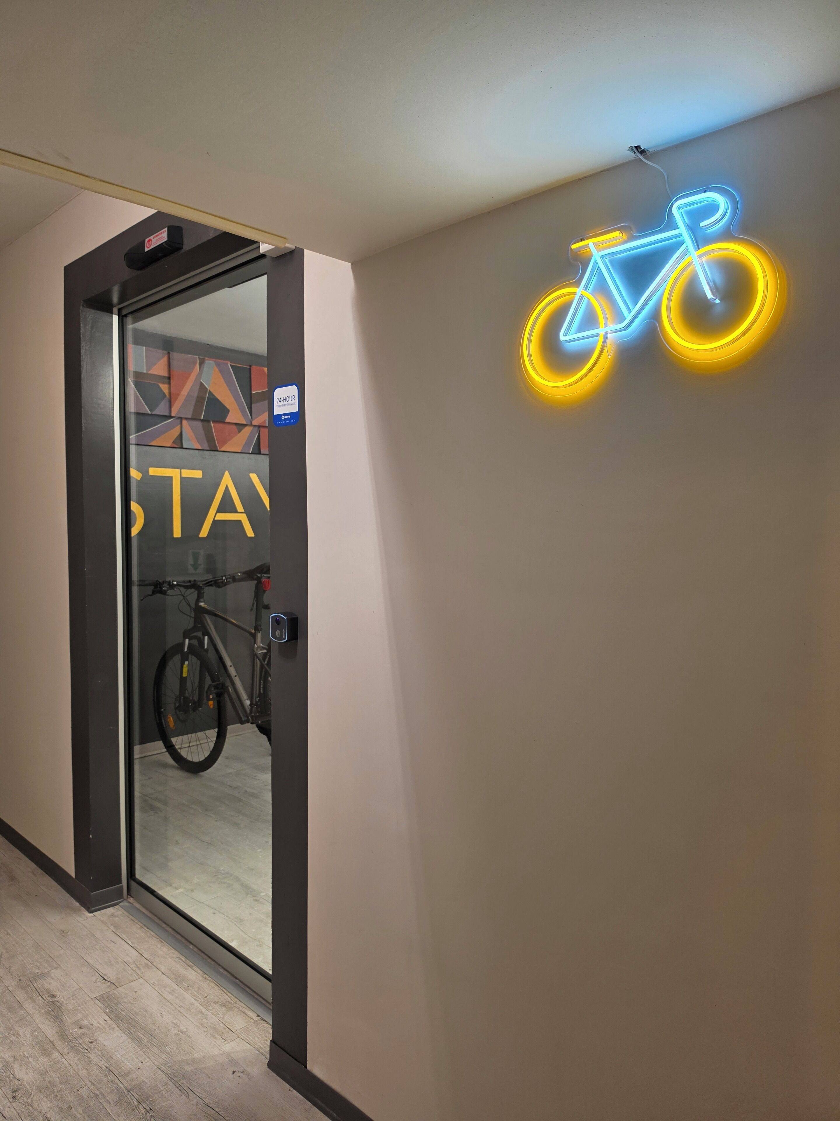 A hotel corridor with a neon bicycle sign, a glass door with a bike rack, and a 'STAY' sign.