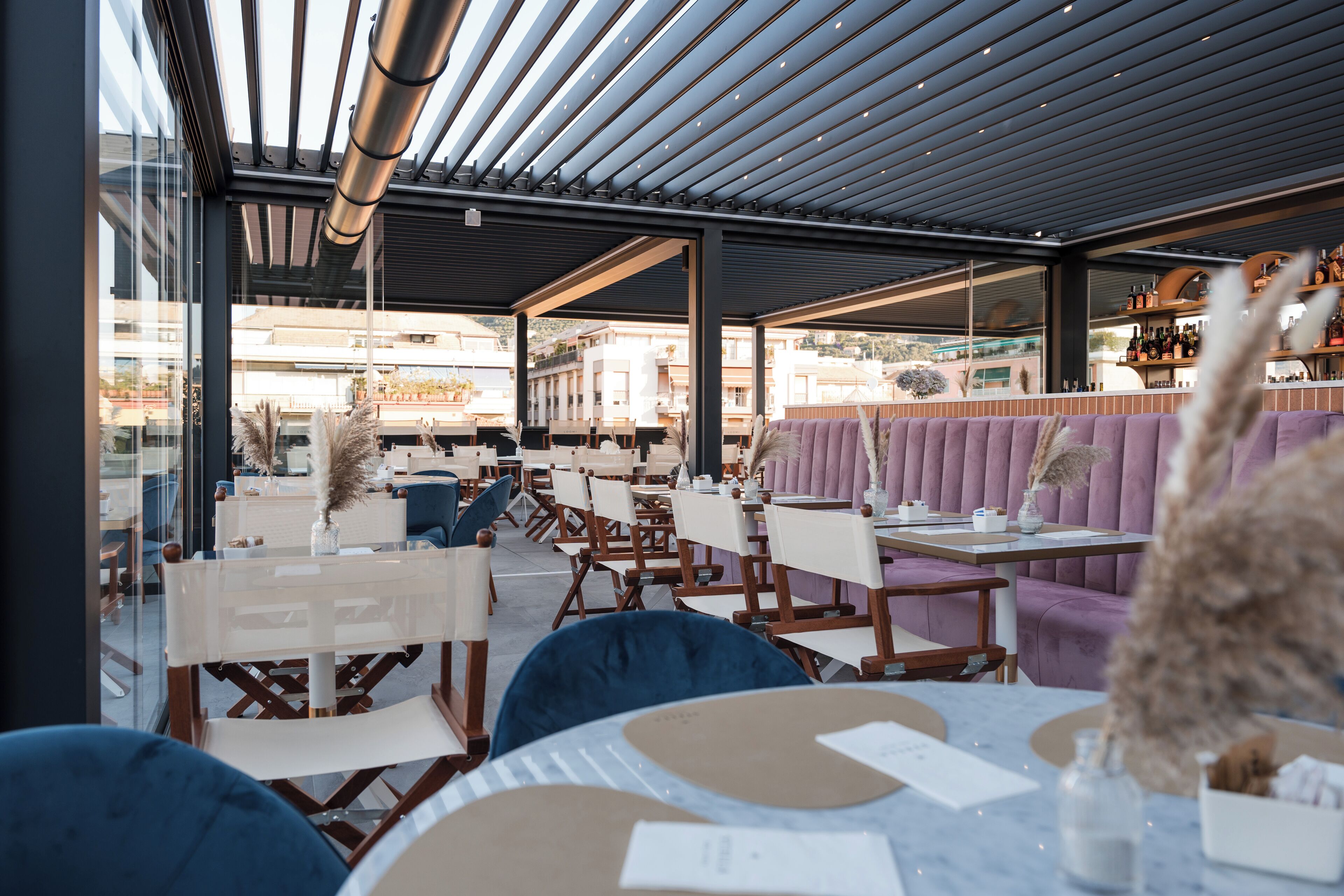 Zona salotto all'aperto con tavoli e sedie, un bar sullo sfondo e vista sugli edifici.