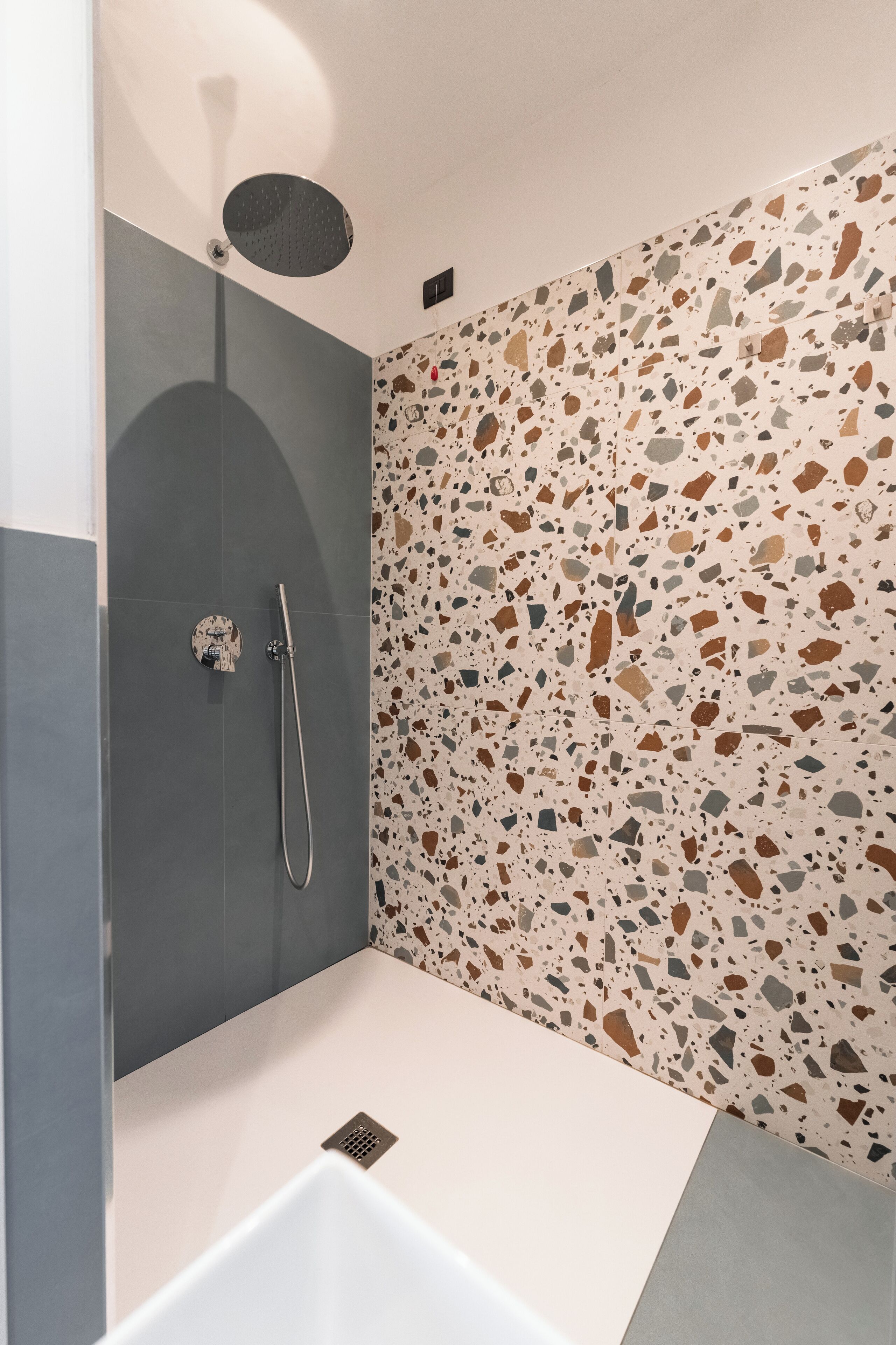 Ein modernes Badezimmer mit Dusche, einer weißen Badewanne und einem Terrazzo-Boden.