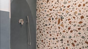 Un baño moderno con ducha, una bañera blanca y suelo de terrazo.