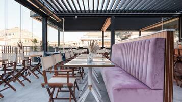 Una moderna zona relax all'aperto con sedie in legno e un divano viola, caratterizzata da una ringhiera in vetro e vista sulla città.